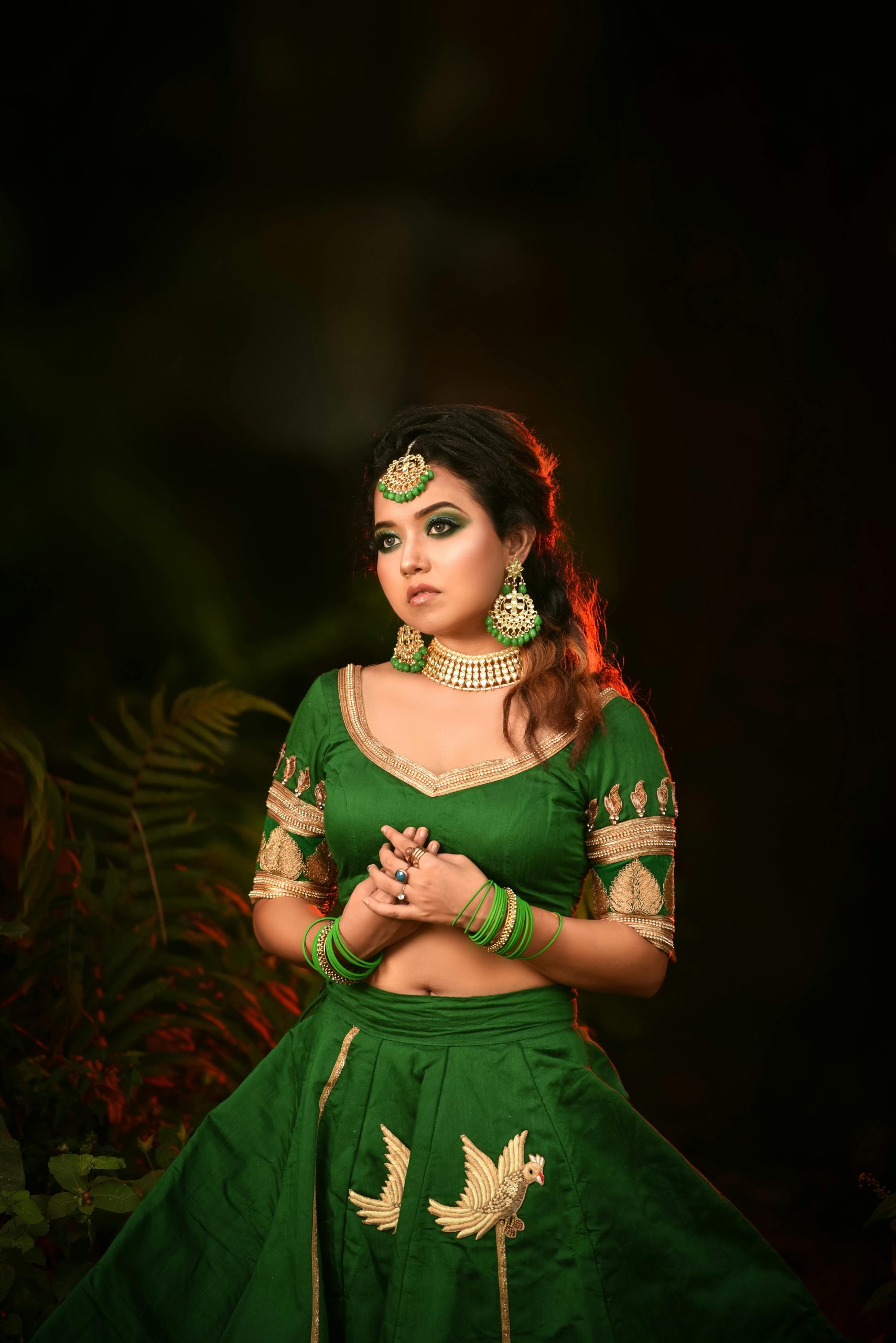 Elegant woman in green traditional Indian dress with jewelry, posing outdoors.
