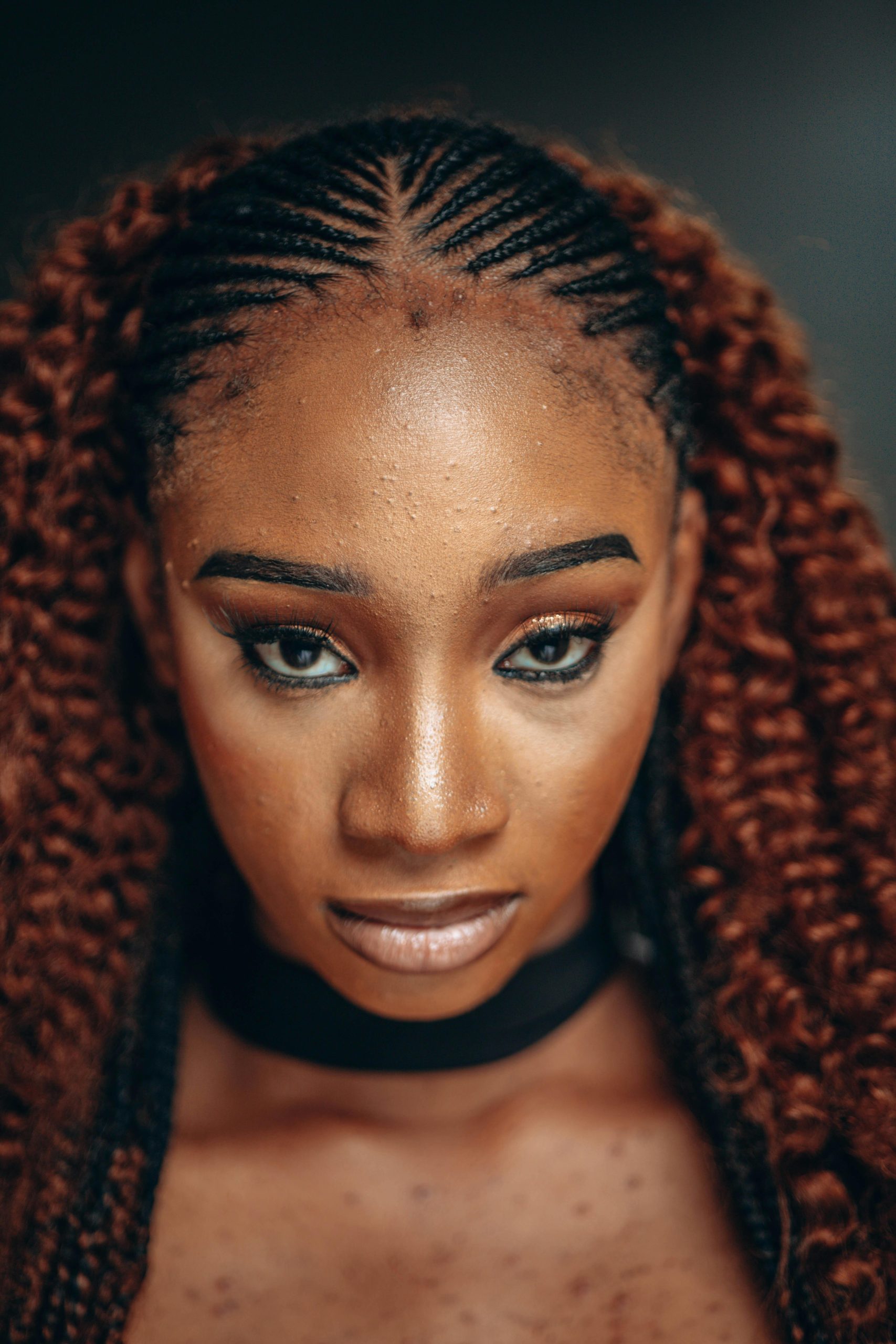 Close-up portrait of a woman with intricate braided hairstyles and a confident expression.