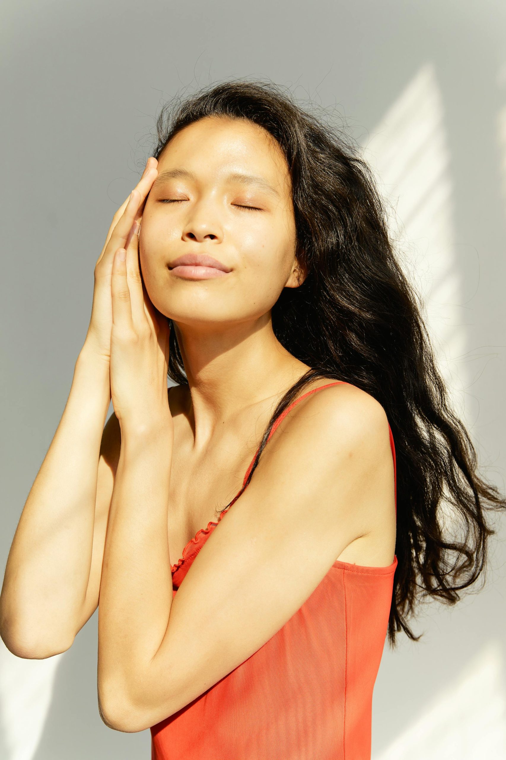 A serene studio portrait of a young woman in a red dress, eyes closed, relaxed pose.